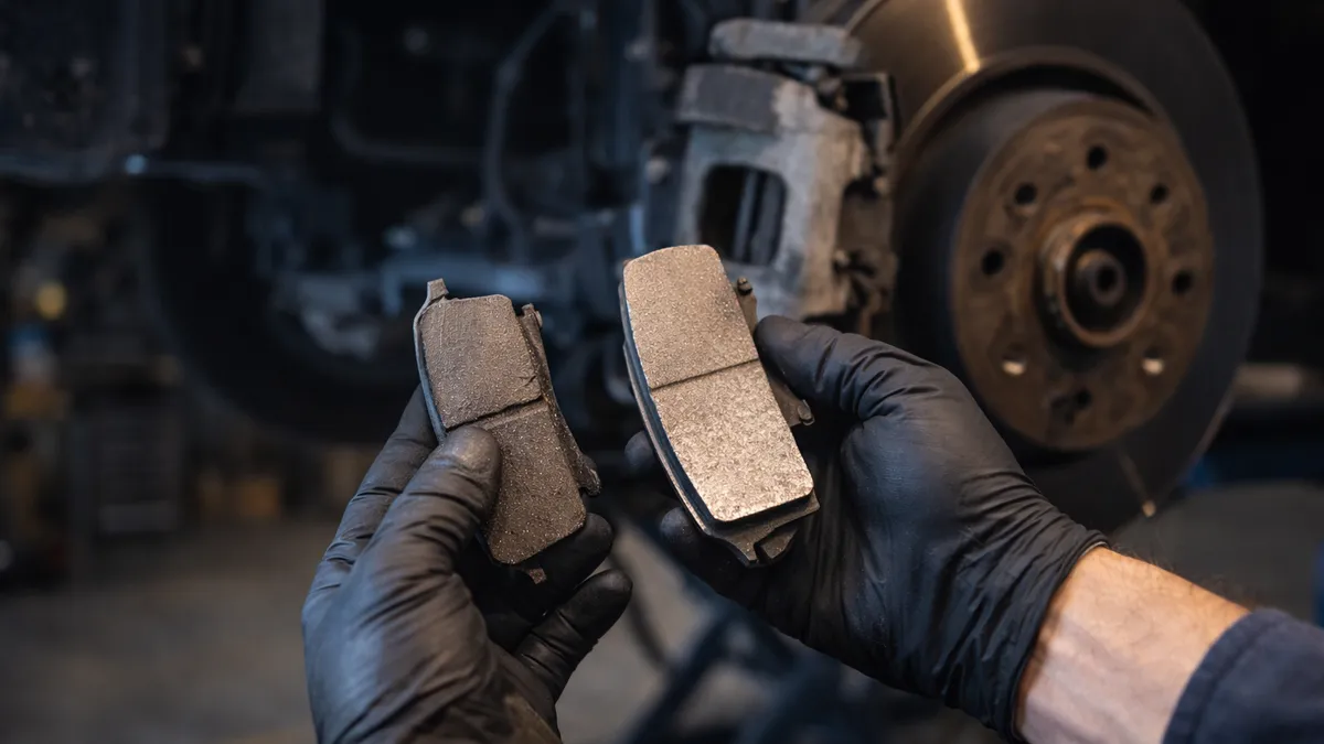 Mechanic comparing a worn thin brake pad to a new thick brake pad